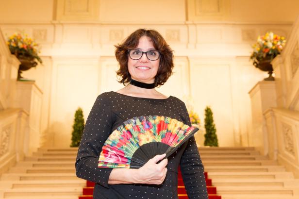 Eine Frau mit Brille und Fächer steht auf einer Treppe.