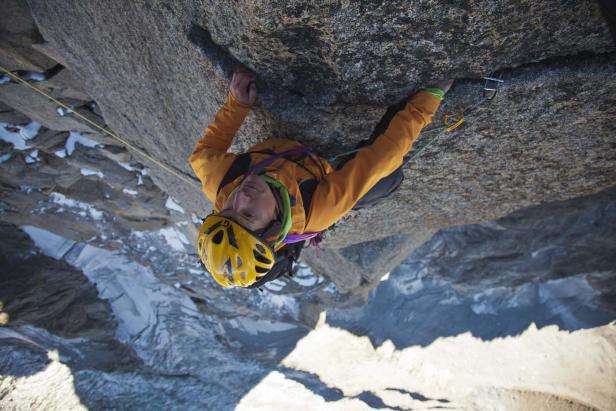 Ein Kletterer hängt an einer Felswand mit Blick auf schneebedeckte Berge.
