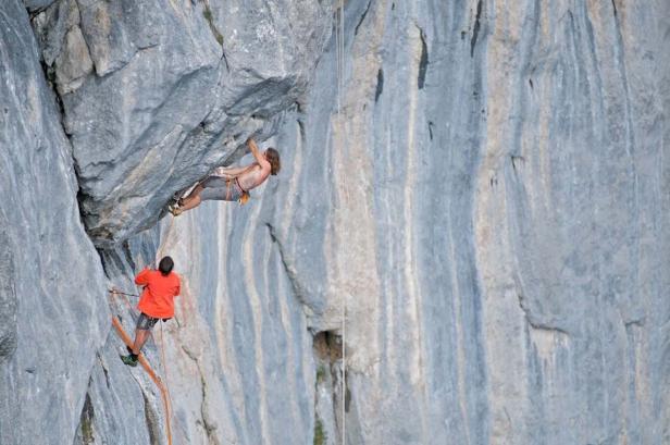 Ein Kletterer hängt an einer Felswand, während ein Sicherer ihn von unten sichert.