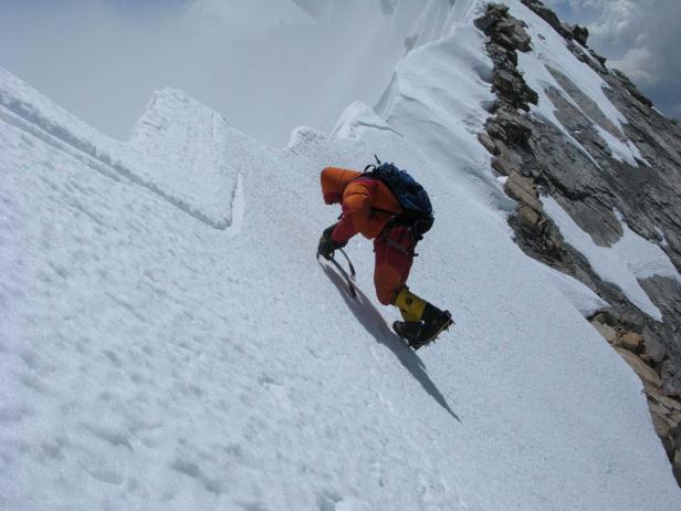 Ein Bergsteiger mit Eispickel überquert einen schneebedeckten Grat.