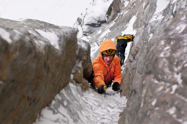 Ein Bergsteiger klettert mit Steigeisen und Eisgeräten eine vereiste Rinne hinauf.