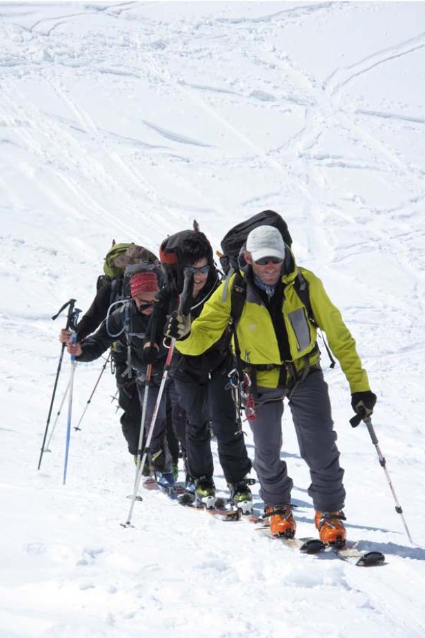 Eine Gruppe von Skibergsteigern steigt einen schneebedeckten Hang hinauf.