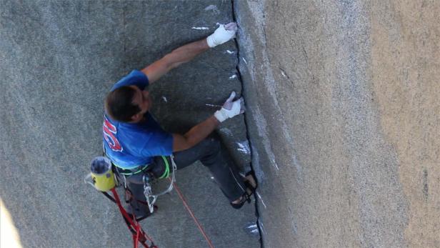 Ein Kletterer mit bandagierten Händen erklimmt eine steile Felswand.