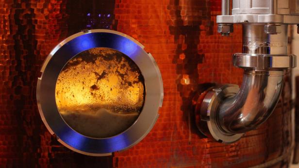 Ein kupferfarbener Braukessel mit einem Schauglas und einem polierten Metallrohr.