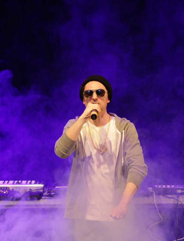 Ein Mann mit Sonnenbrille und Mütze rappt in ein Mikrofon vor einem Keyboard.