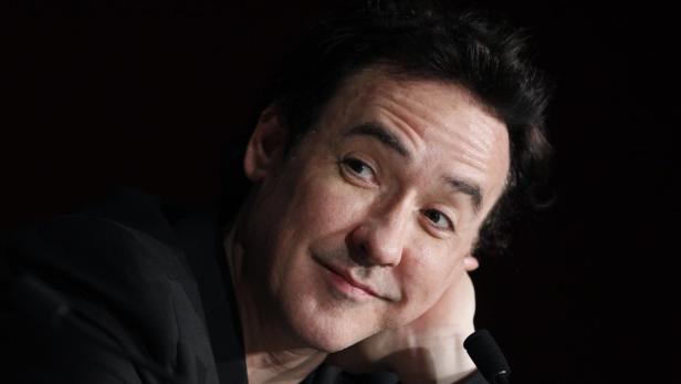 Porträt von John Cusack, der lächelnd in die Ferne blickt.