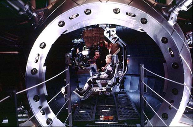 Eine Frau sitzt in einem futuristischen Cockpit, umgeben von technischem Personal.