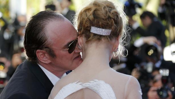 Quentin Tarantino flüstert einer Frau mit blonden Haaren etwas ins Ohr.