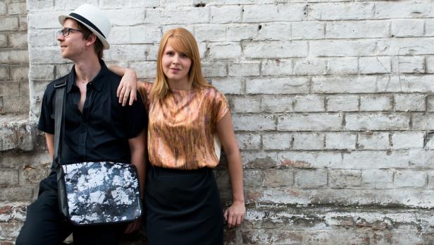 Ein Mann mit Hut und eine Frau lehnen an einer Backsteinmauer.