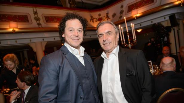 Zwei Männer in Anzügen posieren bei einer Veranstaltung für ein Foto.