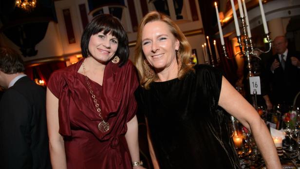 Zwei Frauen posieren lächelnd auf einer Veranstaltung mit Kerzen und festlichen Tischen.