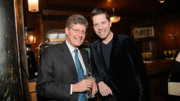 Zwei Männer posieren lächelnd in einer Bar für ein Foto.