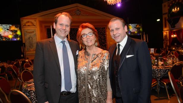 Drei Personen posieren auf einer Gala vor gedeckten Tischen.