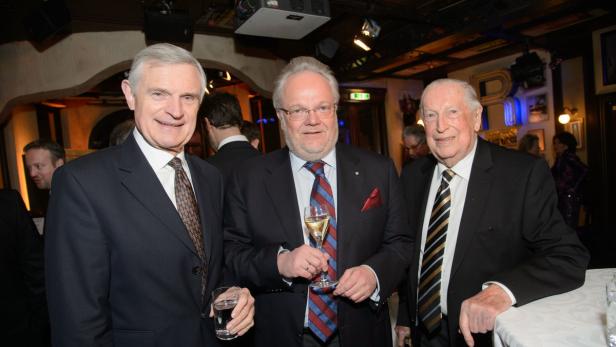 Drei ältere Herren in Anzügen posieren mit Getränken für ein Foto.