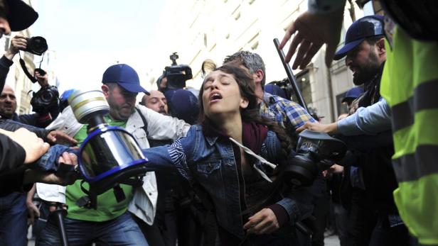 Eine junge Frau wird von mehreren Personen, einige mit Gasmasken, festgehalten.