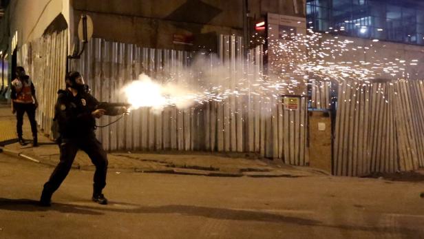 Ein Polizist mit Gasmaske feuert eine Waffe ab, die Funken sprüht.