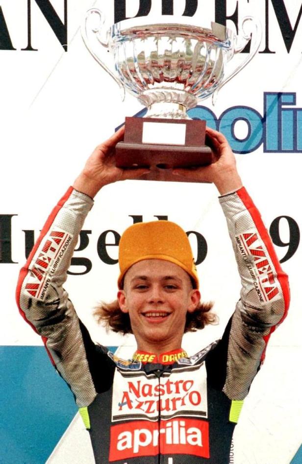 Valentino Rossi hält einen Pokal in die Höhe und lächelt.