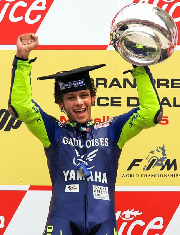 Valentino Rossi feiert mit einer Siegertrophäe und einem Doktorhut auf dem Kopf.