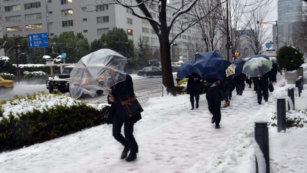 Menschen mit Regenschirmen gehen auf einem verschneiten Bürgersteig in der Stadt.
