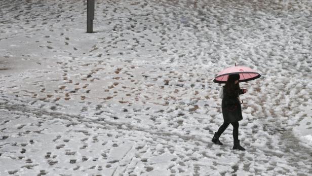 Eine Frau geht mit einem rosa Regenschirm über einen schneebedeckten Platz.