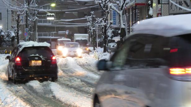 Autos fahren auf einer verschneiten Straße in einer japanischen Stadt.