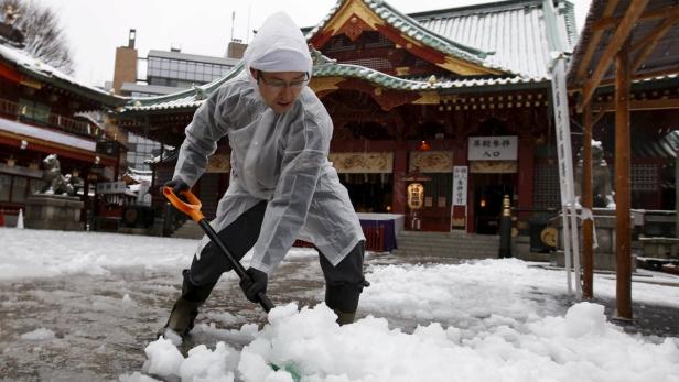 Ein Mann schaufelt Schnee vor einem traditionellen japanischen Gebäude.