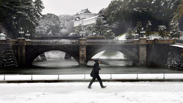 Eine Person mit Regenschirm geht im Winter vor einer Brücke und einem Gebäude in Japan entlang.
