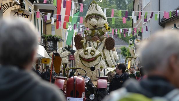 Ein blumengeschmückter Festwagen mit einer Schnecken- und Zwergenfigur fährt durch eine Stadt.