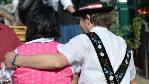 Ein Paar in Tracht sitzt nebeneinander, der Mann hat den Arm um die Frau gelegt.