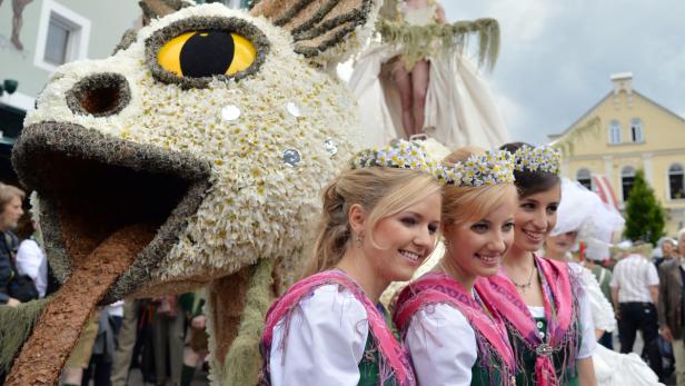 Ein Festumzug mit einem blumengeschmückten Drachen und Trachtenmädchen.
