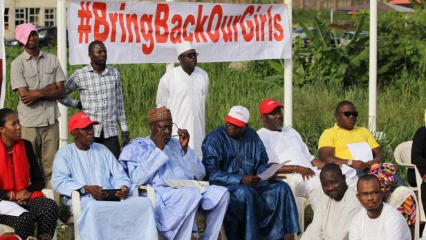 Eine Gruppe von Menschen sitzt unter einem Banner mit der Aufschrift „#BringBackOurGirls“.