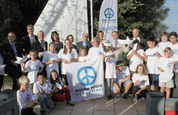 Eine Gruppe von Kindern und Erwachsenen posiert mit Papierbooten und einem Friedensbanner.