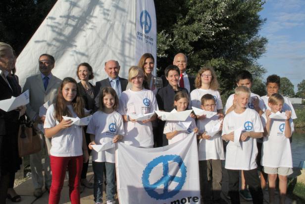 Eine Gruppe von Kindern und Erwachsenen posiert mit Papierbooten und einem Friedensbanner.