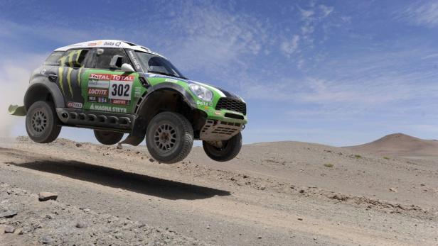 Ein Mini Cooper Rallye-Auto springt über eine Sanddüne.