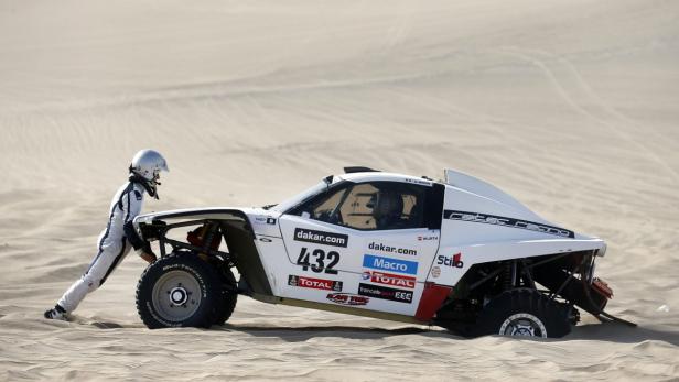 Ein Rennfahrer schiebt einen weißen Race-Buggy mit der Nummer 432 im Sand an.