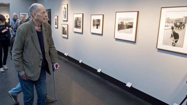 Ein älterer Mann mit Gehstock betrachtet Fotografien in einer Kunstgalerie.