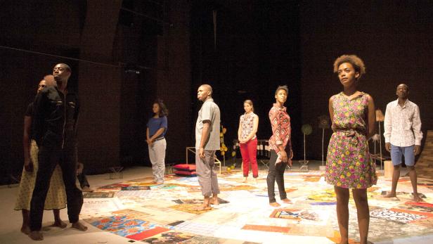 Eine Gruppe von Schauspielern steht barfuß auf einer Bühne mit einem Muster aus Bildern.