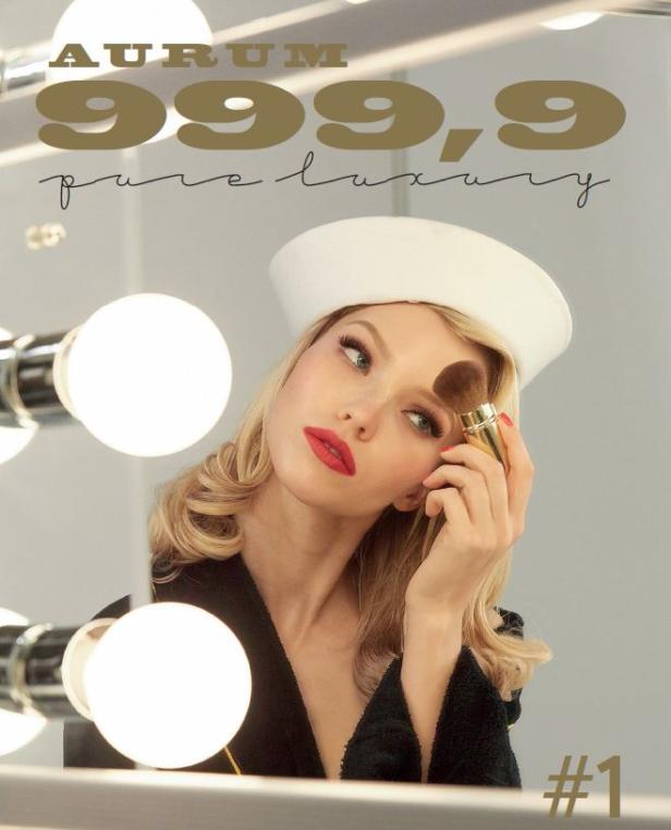 Eine blonde Frau mit rotem Lippenstift schminkt sich vor einem Spiegel mit Glühbirnen.