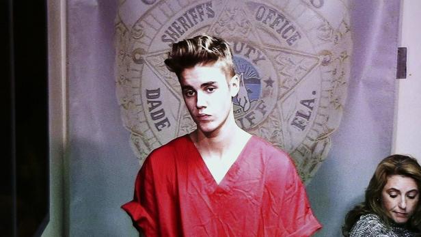 Justin Bieber in einem roten Gefängnisoverall vor dem Abzeichen des Miami-Dade Sheriffs.