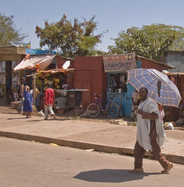 Ein Mann mit Schirm geht eine Straße in einer afrikanischen Stadt entlang.