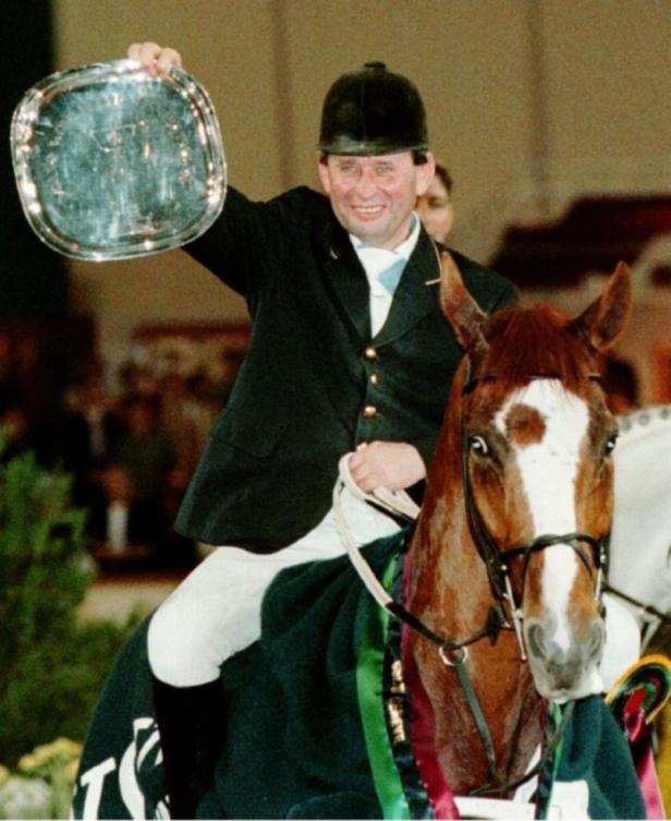 Ein Reiter hält eine silberne Trophäe auf dem Rücken eines Pferdes.