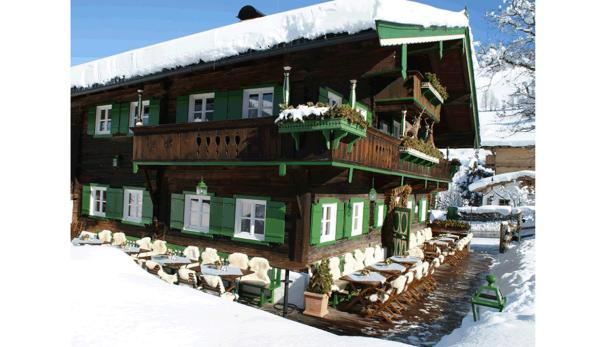Ein traditionelles Holzhaus mit grünen Fensterläden und Schnee auf dem Dach.