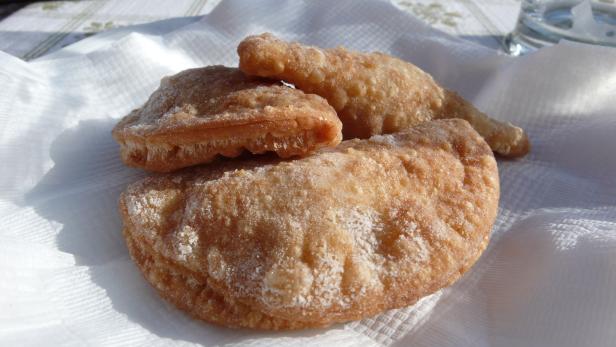 Drei frittierte Teigtaschen liegen auf einer weißen Serviette.