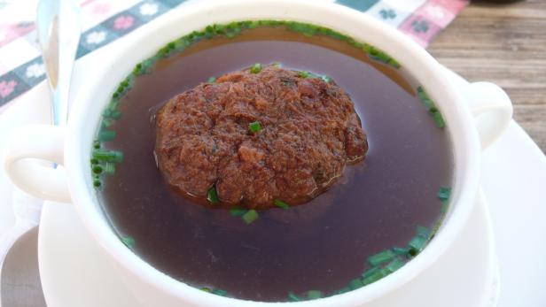 Eine Suppe mit einem großen Leberknödel und Schnittlauch in einer weißen Tasse.