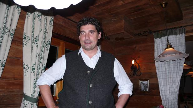 Ein Mann in Trachtenweste steht in einem holzvertäfelten Raum.