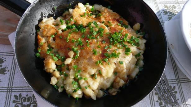 Käsespätzle mit Schnittlauch in einer schwarzen Pfanne serviert.