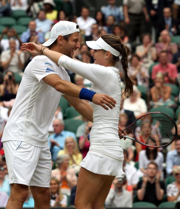 Ein Tennis-Mixed-Doppel-Team umarmt sich vor einem applaudierenden Publikum.