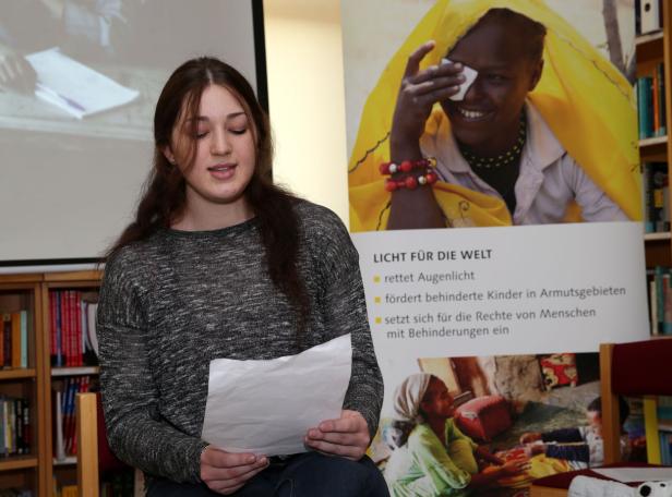 Eine junge Frau liest vor einem Plakat von „Licht für die Welt“.