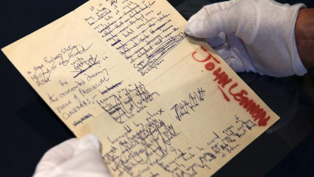 Ein handschriftliches Manuskript von John Lennon wird von einer Person mit Handschuhen gehalten.