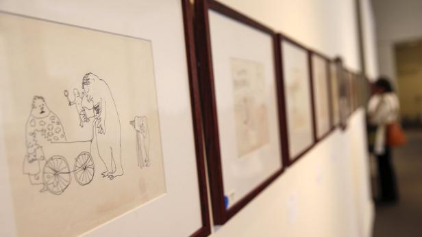 Eine Reihe gerahmter Zeichnungen hängt an einer weißen Wand in einer Kunstgalerie.